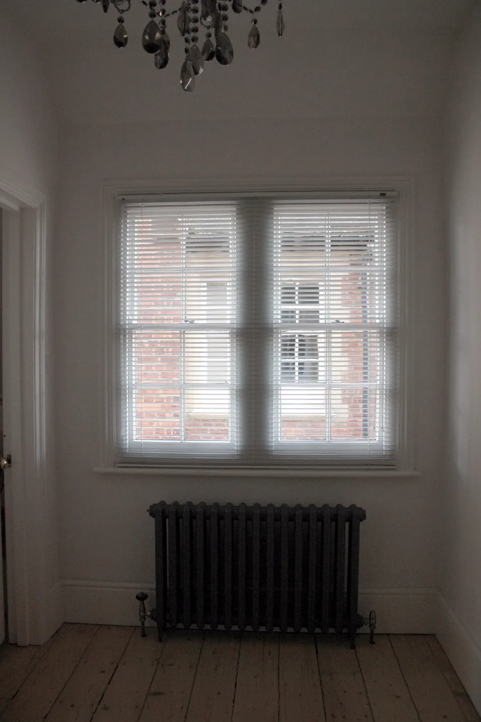 A room with bare timber floorboards and a cast-iron column radiator before works